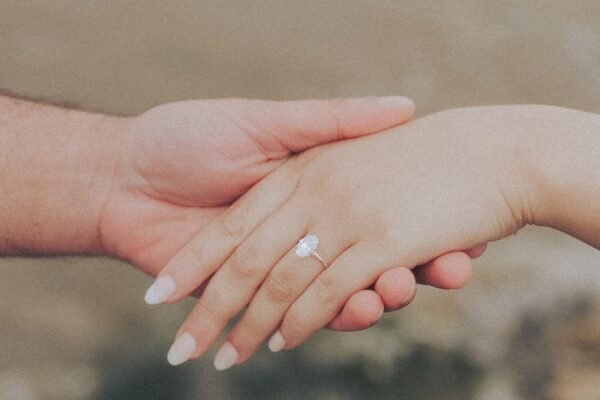 Close-up of a couple holding hands with an engagement ring by the beach.
