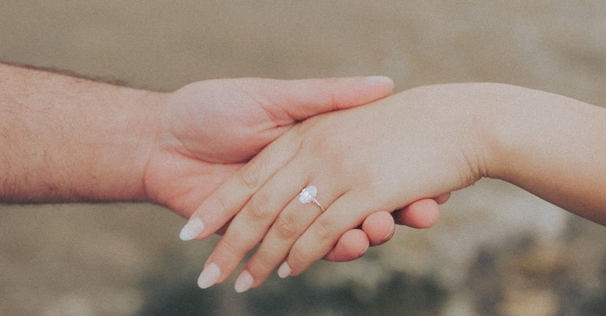 Close-up of a couple holding hands with an engagement ring by the beach.