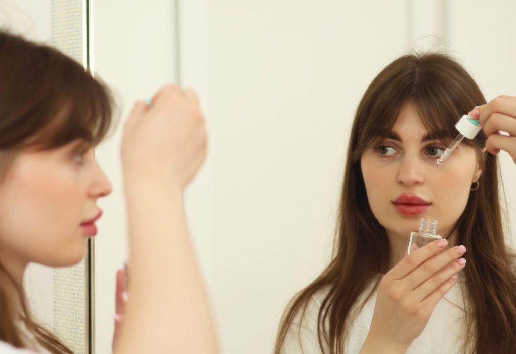 A young woman applying skincare serum in front of a mirror indoors. Perfect for beauty and self-care themes.